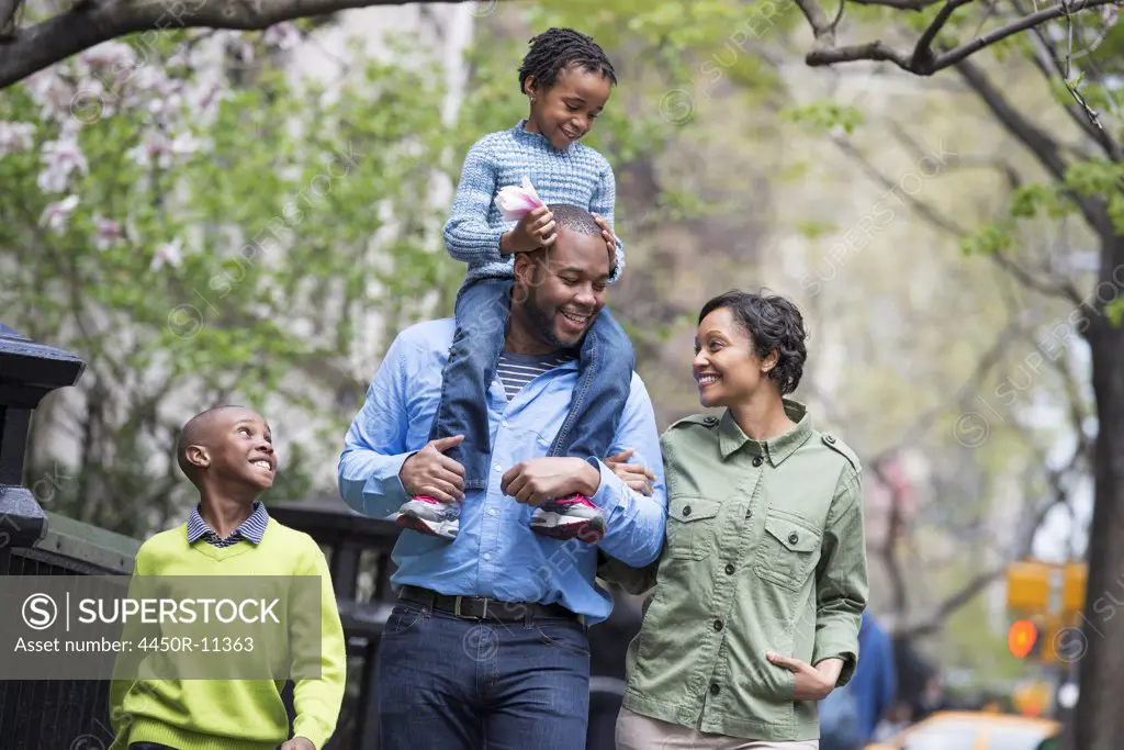 A New York city park in the spring. A family, parents and two boys.  A child riding on his father's shoulders. New York city, USA