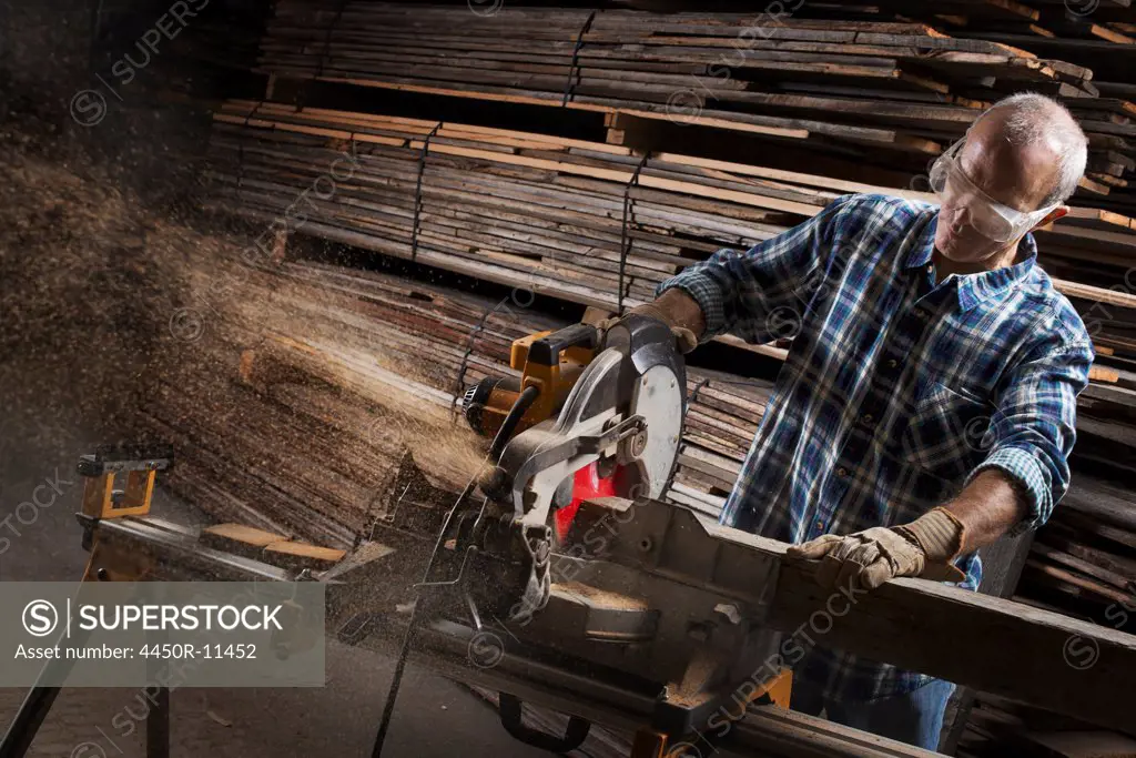 A reclaimed lumber workshop. A man in protective eye goggles using a circular saw to cut timber.  Pine Plains, New York, USA
