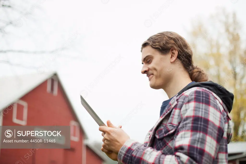 A young man using a computer tablet, a portable PC tablet device, on an organic farm. Woodstock, New York, USA