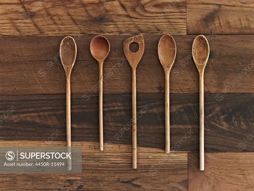 Home cooking. A wooden table with a varied wood grain and colour. Five wooden spoons in a row.  New York, USA