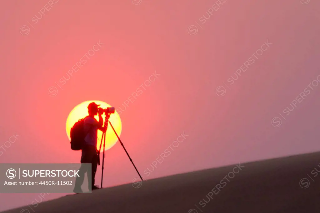 Photographer silhouetted in the setting sun in the Namib Desert, Namibia Namib Desert, Namibia