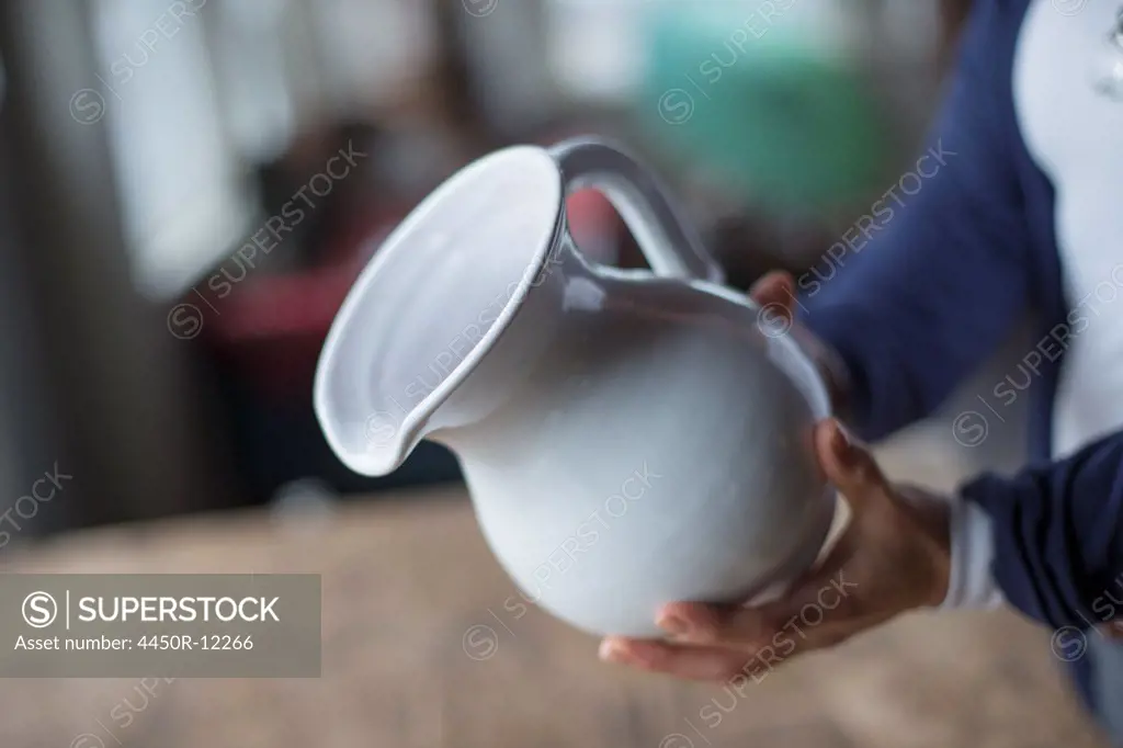A woman holding a white pottery jug in an antique goods and furniture store.  High Falls, New York, USA