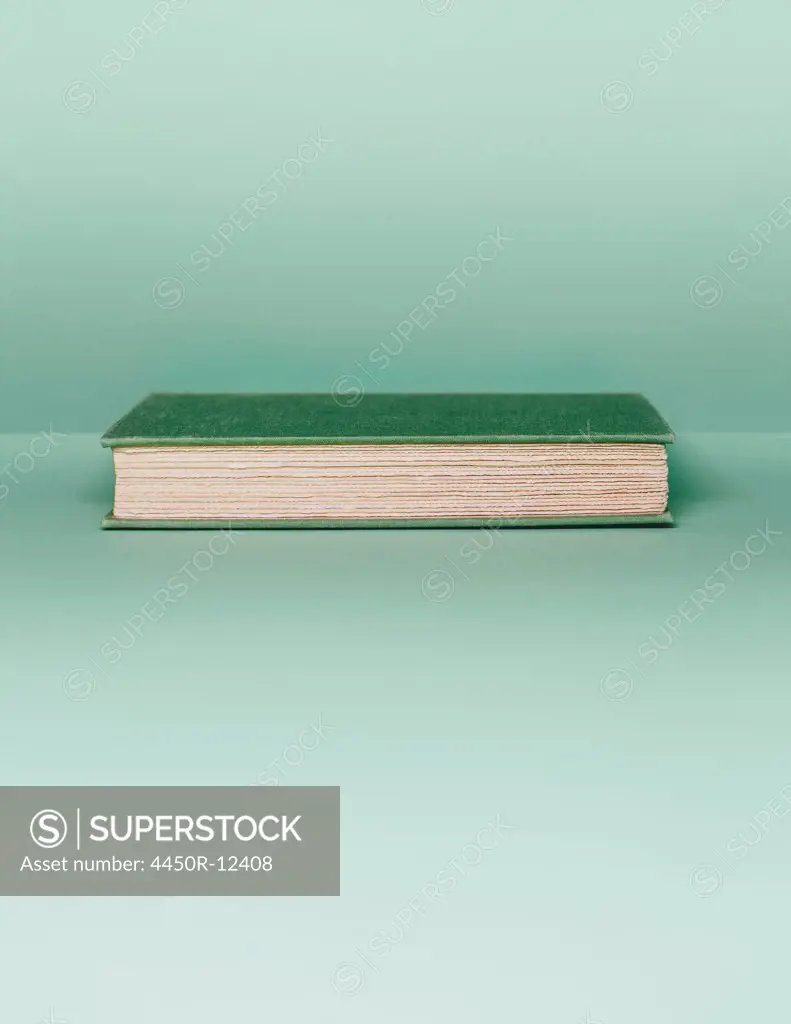 A hard cover book with a green cover, and white paper page edges, lying horizontal on a pale green background.