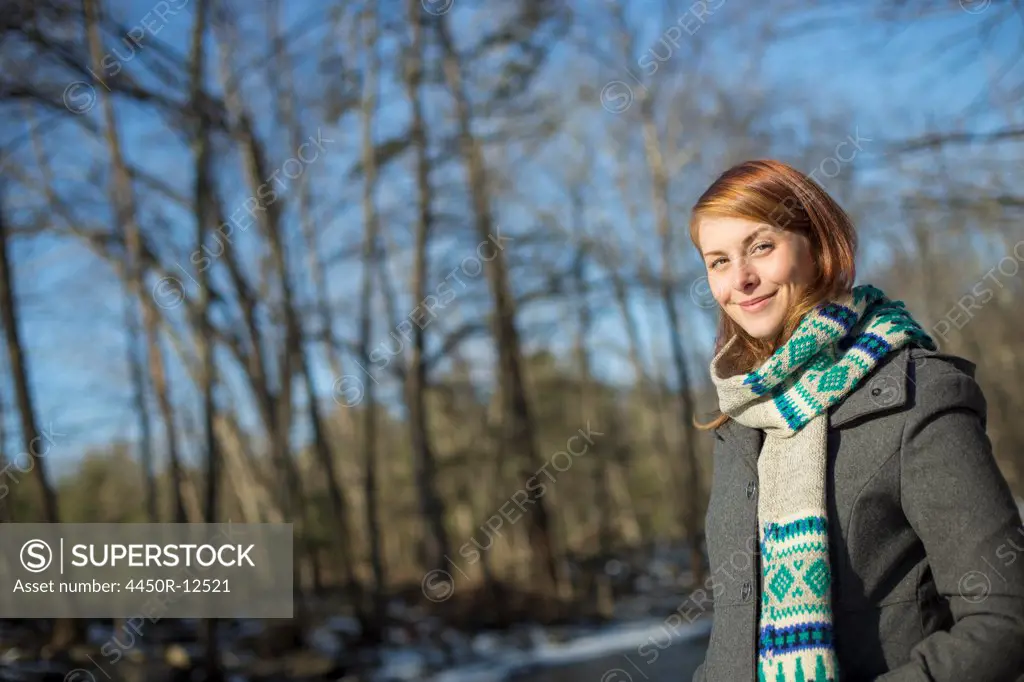 A young woman in a woodland on a winter day.  Wearing a bright knitted patterned scarf. Woodstock, New York, USA
