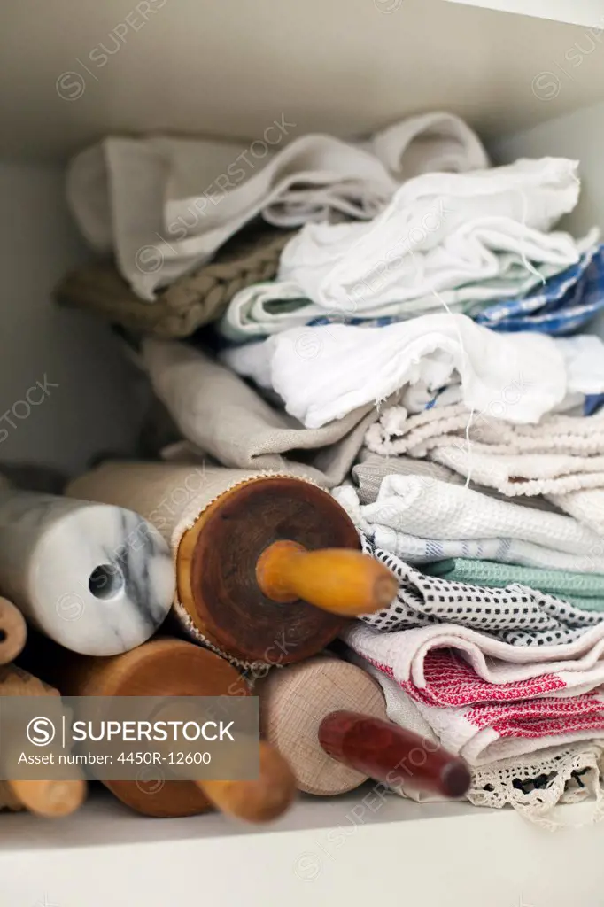 A shelf piled high with cloths, linen and a small stack of rolling pins or wooden spindles. Rome, Italy