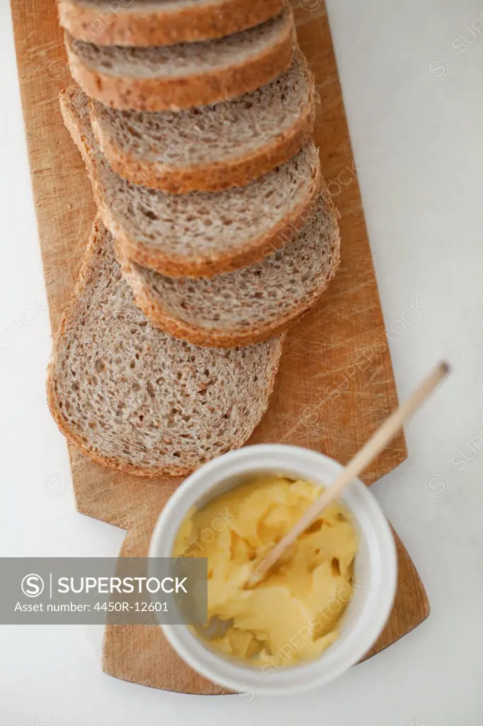A wooden breadboard with a sliced brown loaf laid out. A dish of butter with a wooden butter knife.  Rome, Italy