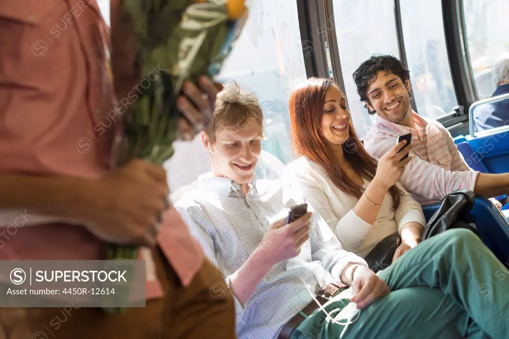 Urban Lifestyle. A group of people, men and women on a city bus, in New York city. Two people checking their phones. One man standing holding a bunch of flowers. New York City, USA