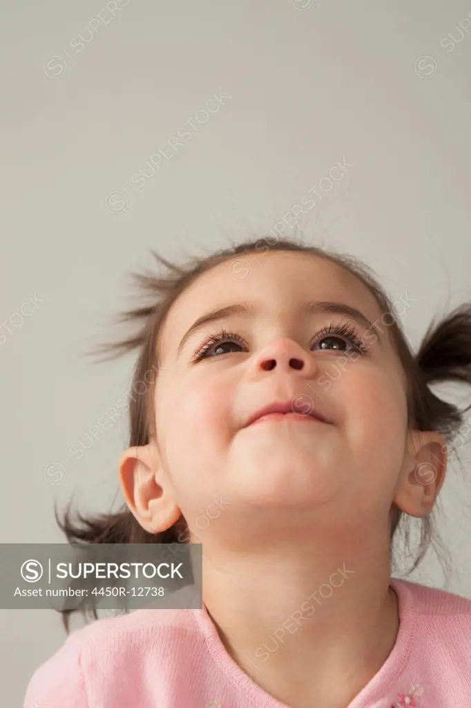 A young girl with brown eyes and dark hair in bunches. Looking upwards with her head thrown back.  Sante Fe, New Mexico, USA