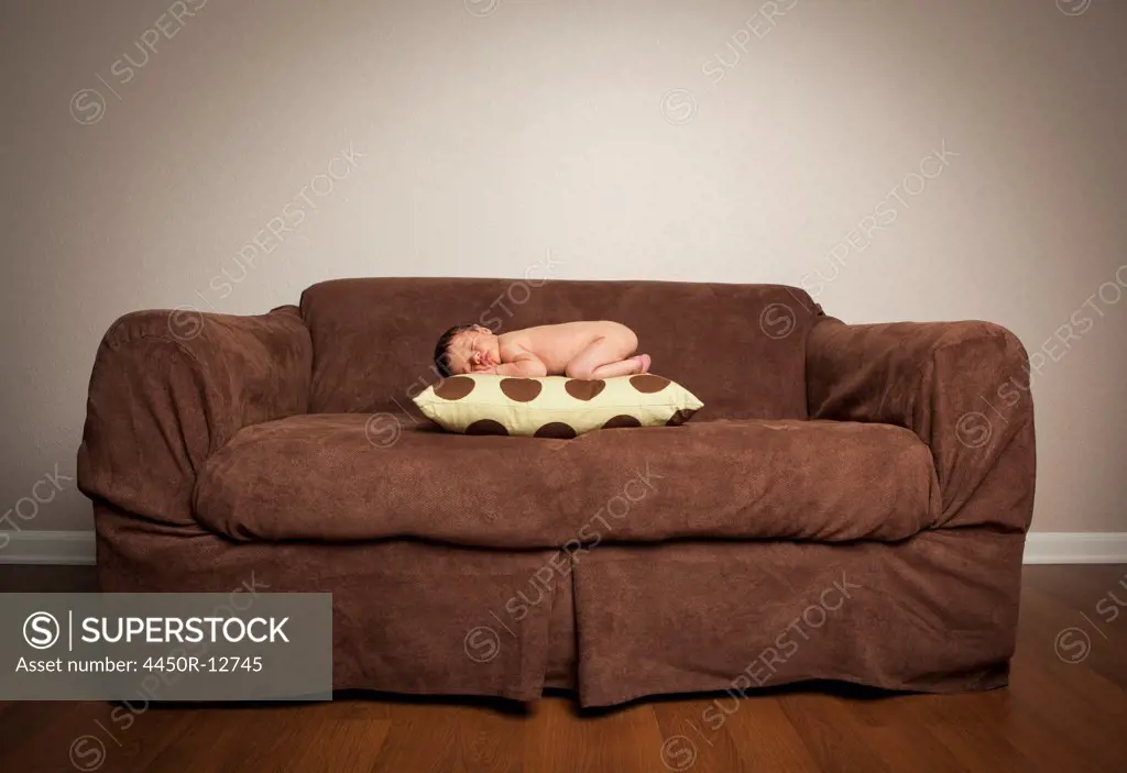 A naked newborn baby lying on his front, sleeping on a pillow on a brown couch. Sante Fe, New Mexico, USA