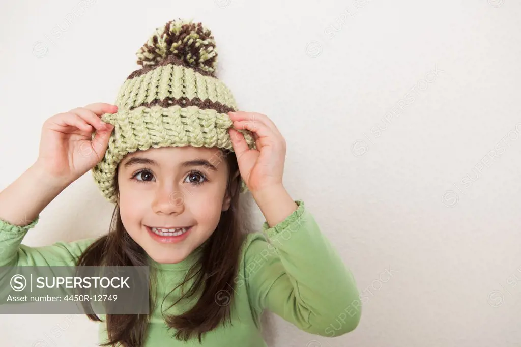 A young child with long brown hair, wearing a knitted hat with a pompom, peering from underneath the brim.  Sante Fe, New Mexico, USA