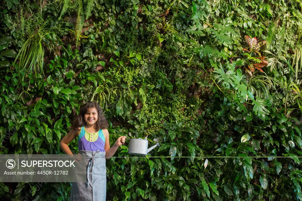 A young girl standing in front of a wall covered with ferns and climbing plants.  New York City, USA