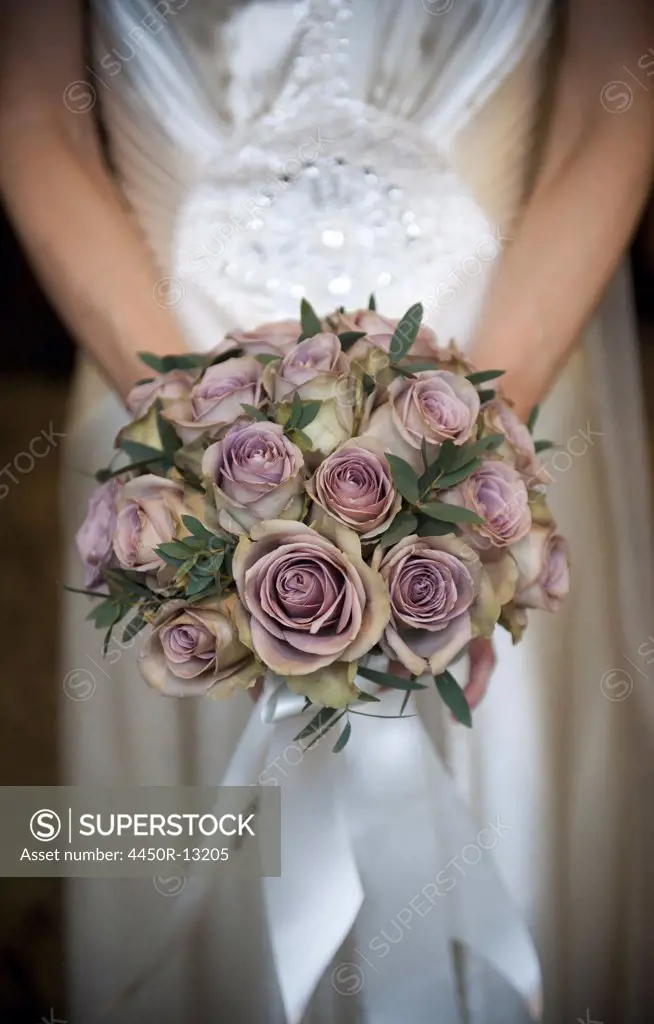 A bride in a white dress, holding a bridal bouquet of pastel coloured roses. England. 02/19/2011