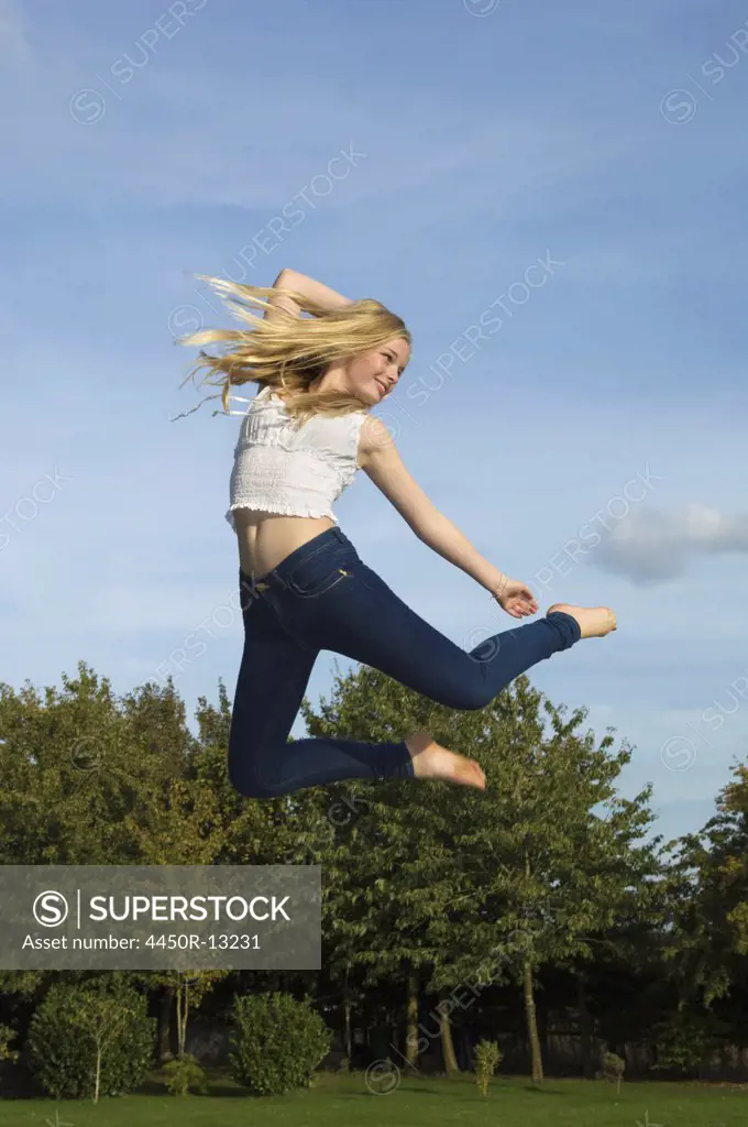 Teenage girl with long blond hair jumping in the air. Gloucestershire, England. 09/15/2011