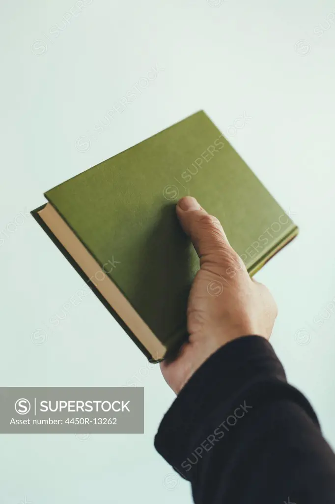 A man's hand holding an old green hardback book. King County, Washington, USA. 12/04/2013