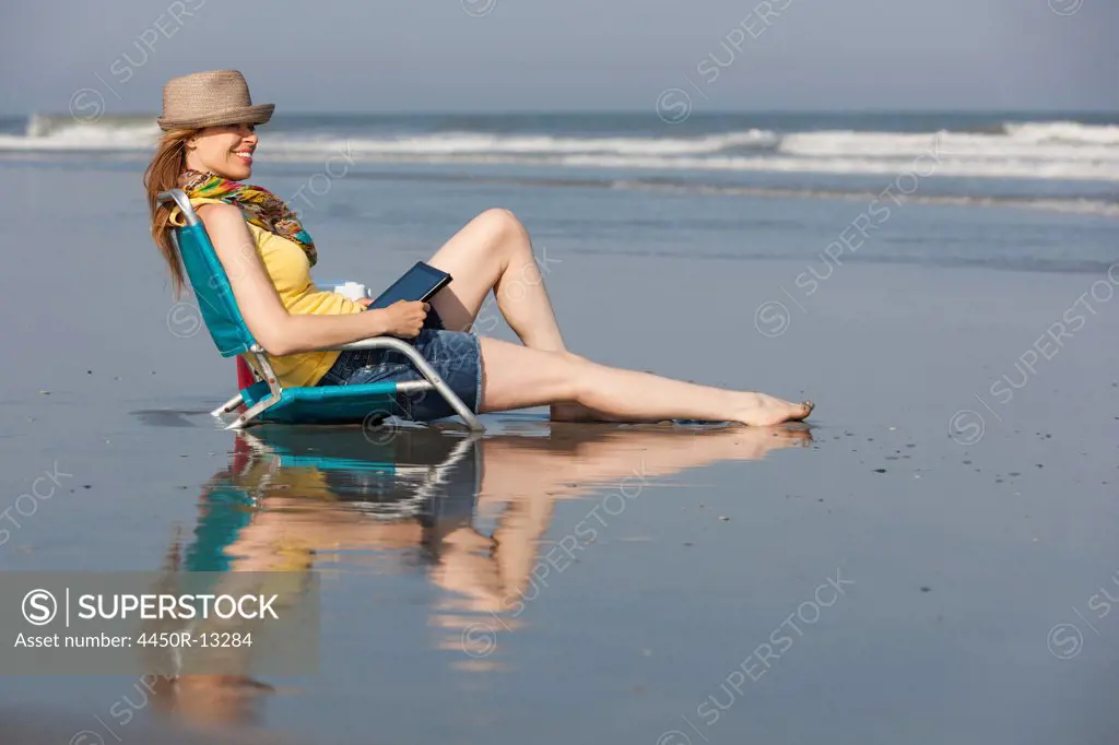 A woman in a sunhat and scarf on the beach on the New Jersey Shore, sitting holding a digital tablet.  Ocean City, New Jersey, USA. 06/28/2012