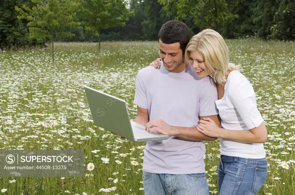 A man and woman in a flower meadow, looking at a laptop screen. England. 06/08/2007