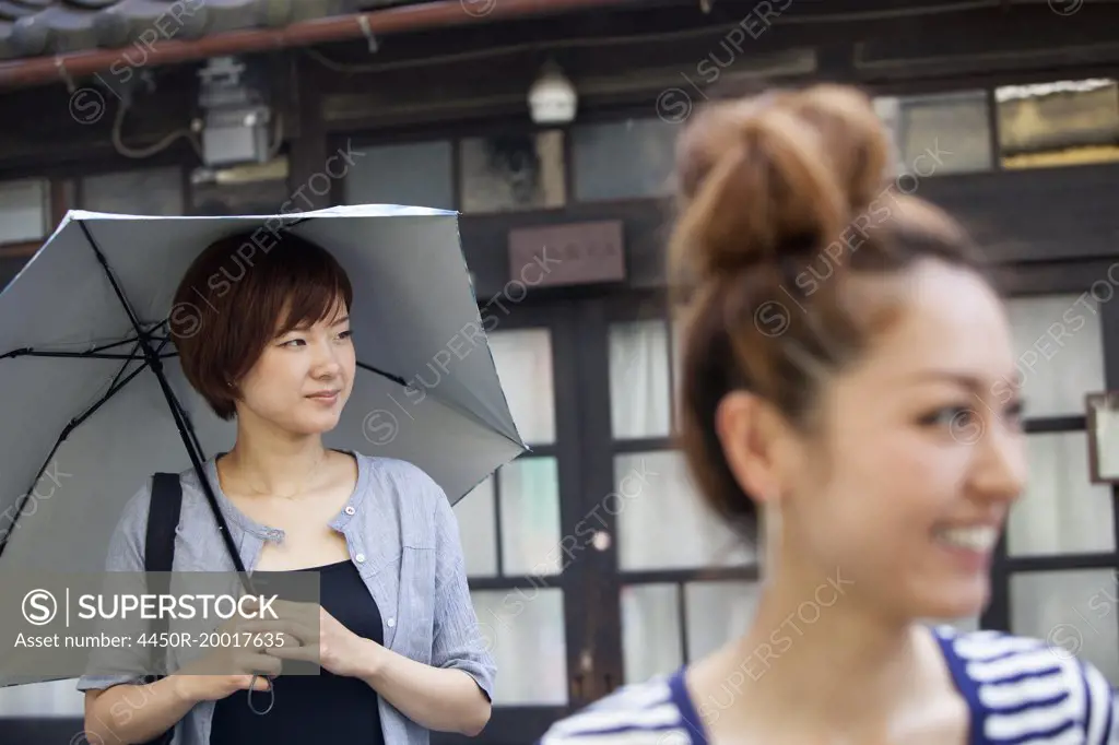 Two women standing outdoors, one holding an umbrella.