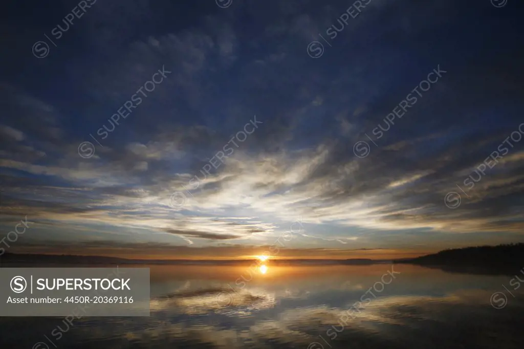 The sun on the horizon, seen over the waters of a lake. Dawn.