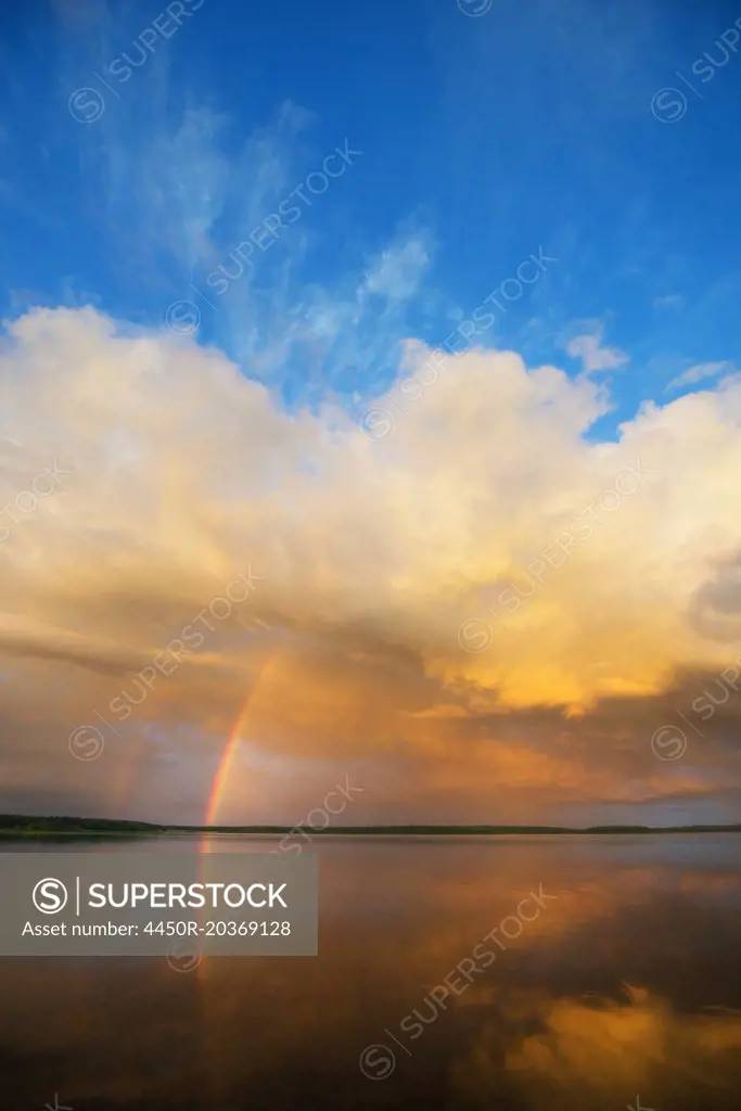 A rainbow and a dramatic cloud formation over a lake.