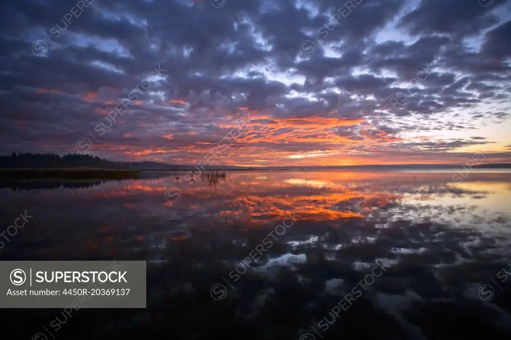 Sunset sky reflected in a lake, and clouds in the sky.