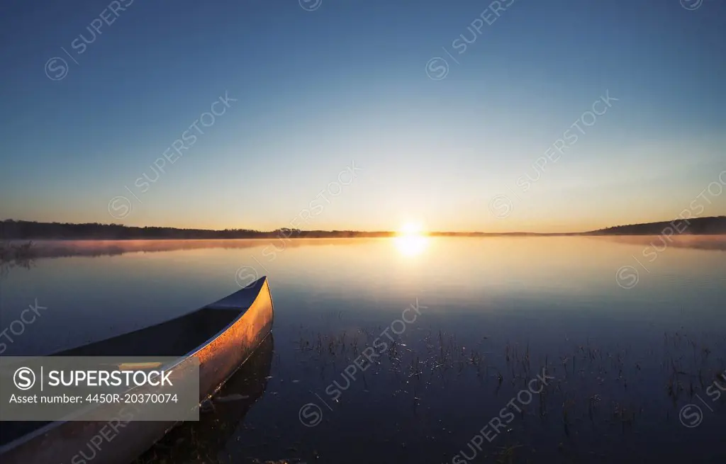 A canoe on a flat calm lake at sunset.