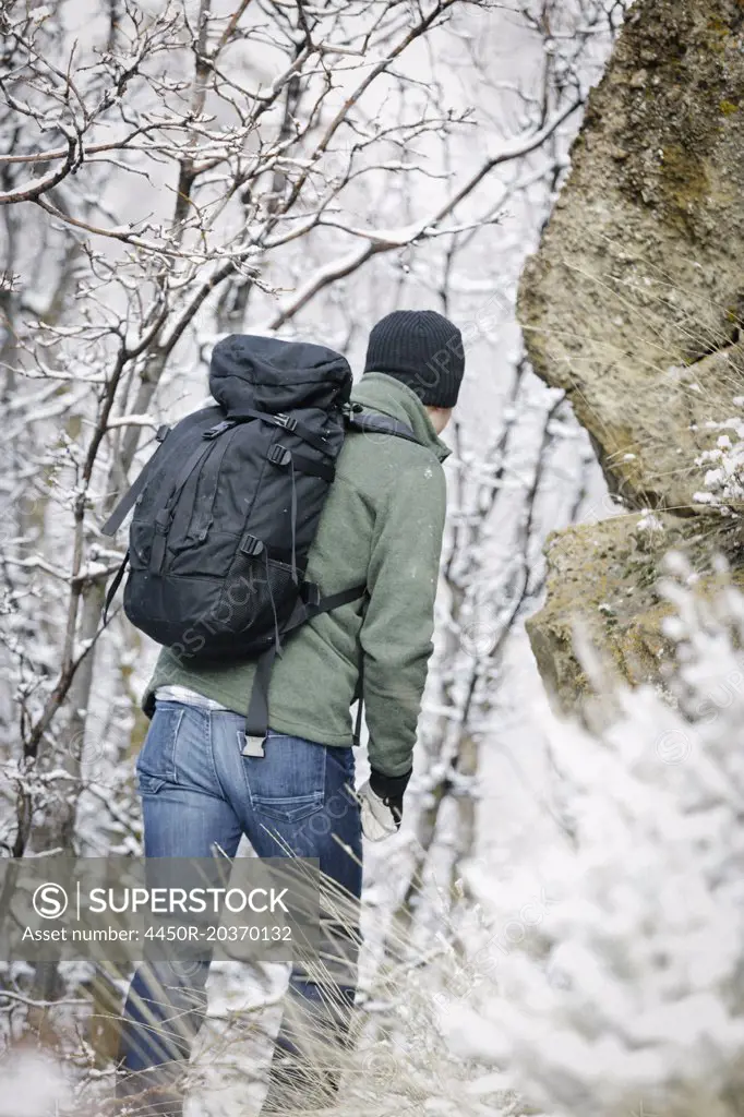 A man wearing a fleece jacket and hat, carrying a rucksack, climbing up a rocky slope.