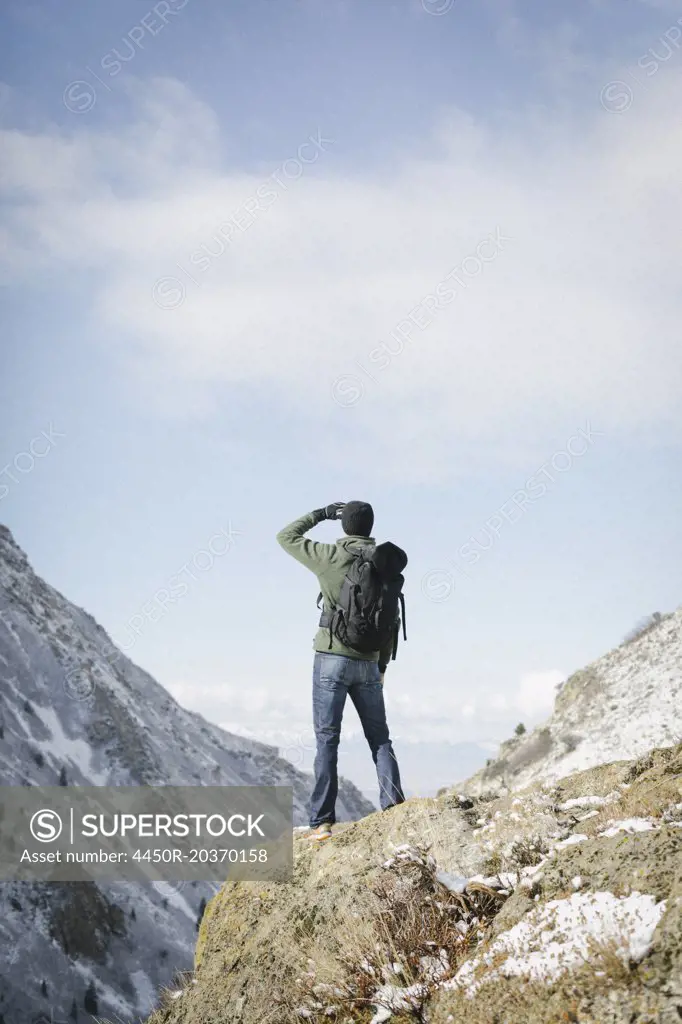 A man hiking in the mountains standing on an outcrop looking at the view.