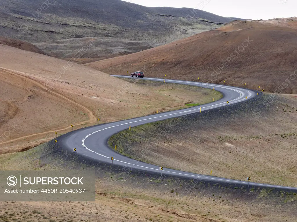 A red car on a winding road through the mountains.