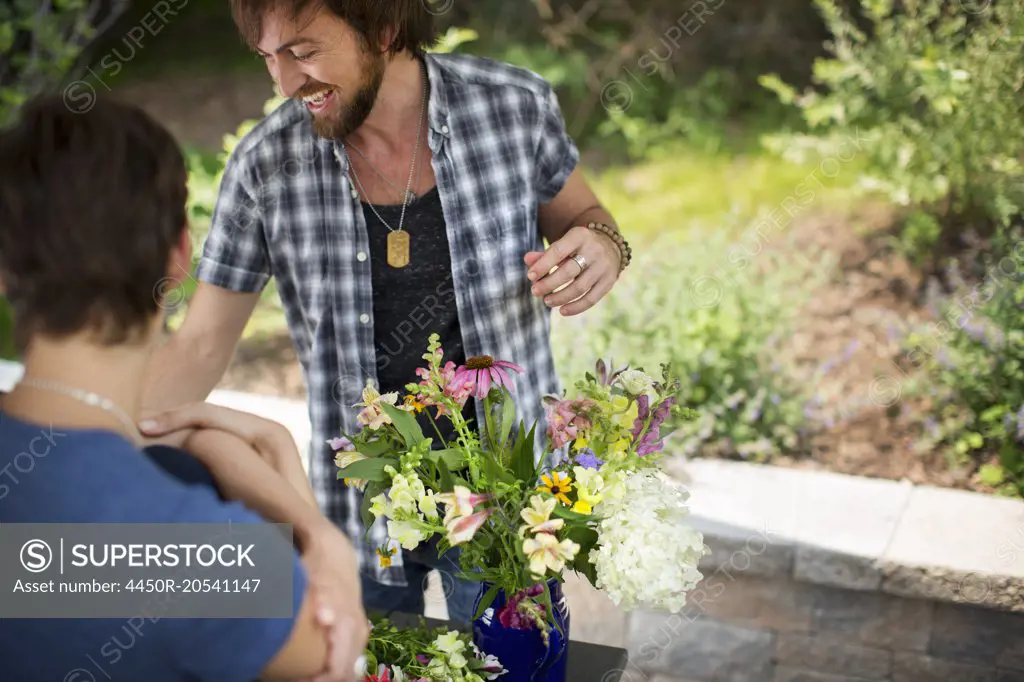 A man and woman standing by a table and a large vase of flowers.