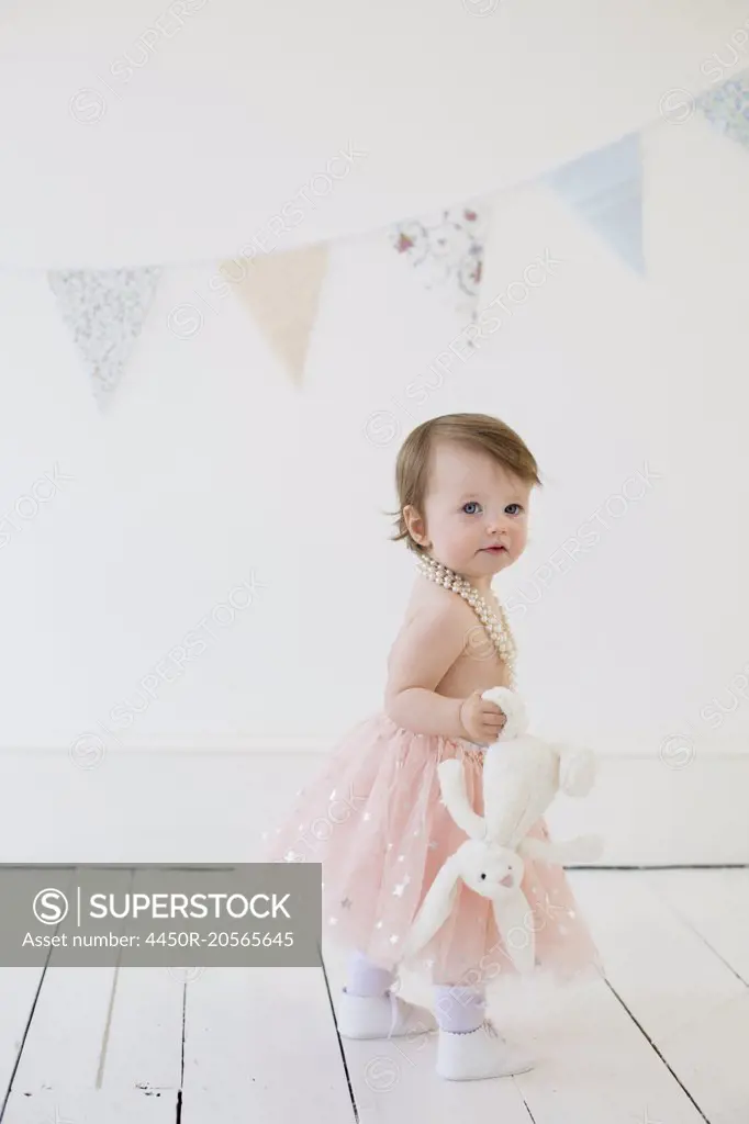Young girl holding a cuddly toy, standing in a photographers studio, posing for a picture.