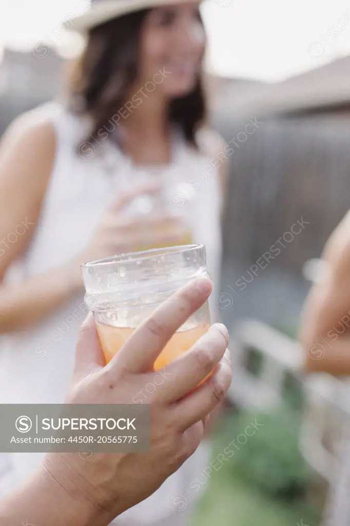 Close up of a hand holding a drink, a woman in the background.