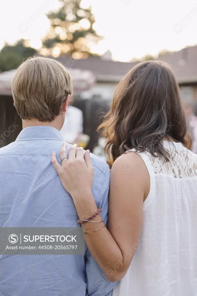 Rear view of a couple standing side by side in a garden, woman touching man's shoulder.