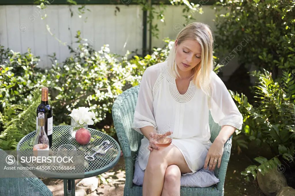Blond woman sitting in a garden in summer, holding a wine glass.