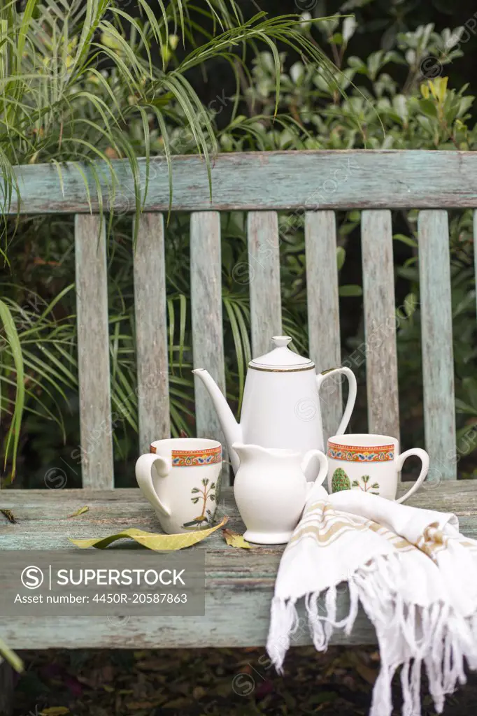 Coffee pot and mugs on a wooden garden bench.