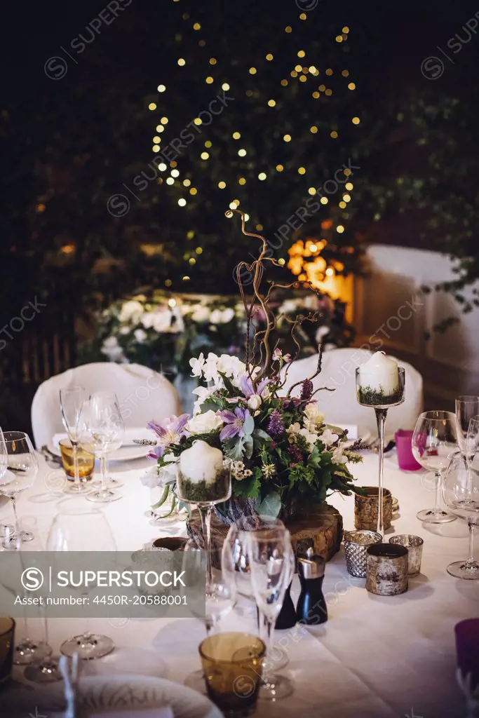 A table laid for a special occasion, with a floral centrepiece and candles, at night.