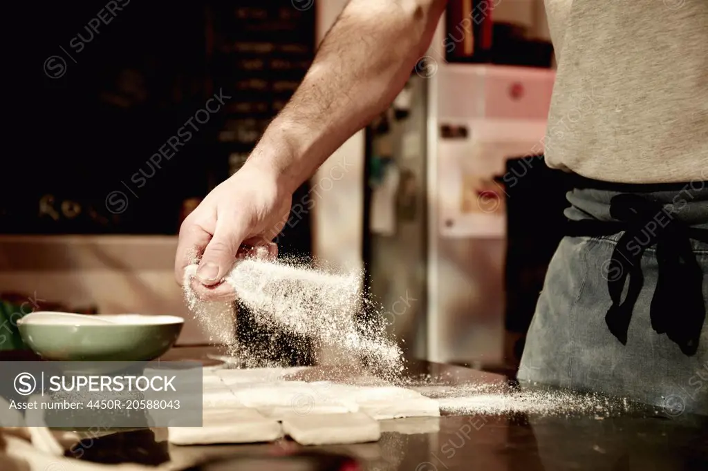A baker working on a floured surface, dividing prepared dough into squares.