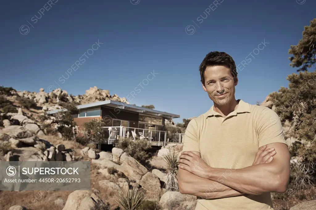 A man standing in front of an eco home, designed to blend into the rocky hilllside of a desert landscape. Sustainable architecture with a low impact.