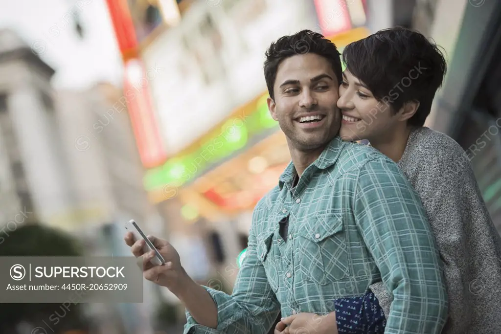 A couple, man and woman hugging on a city street. Man holding a smart phone.