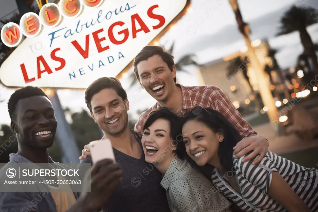 A group of five friends, men and women posing under the Las Vegas sign.