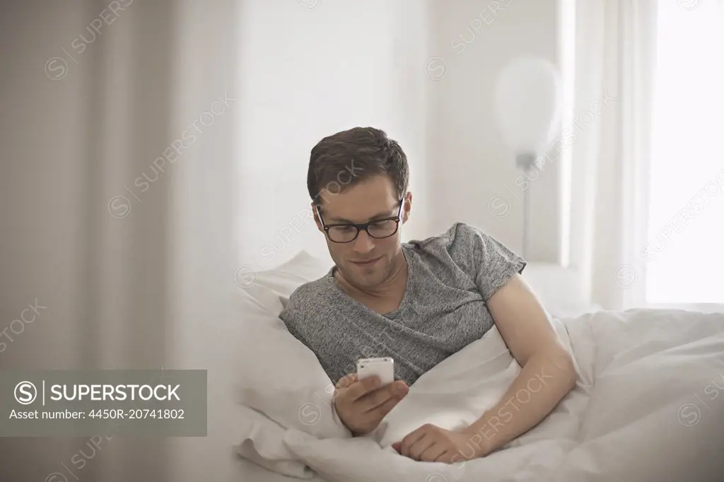 A man lying in bed checking his messages on his phone.
