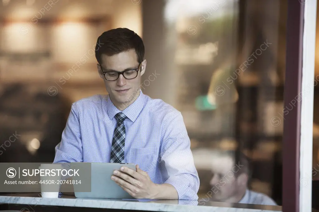 A working day. Businessman in a shirt and tie seated using a digital tablet in a cafe.