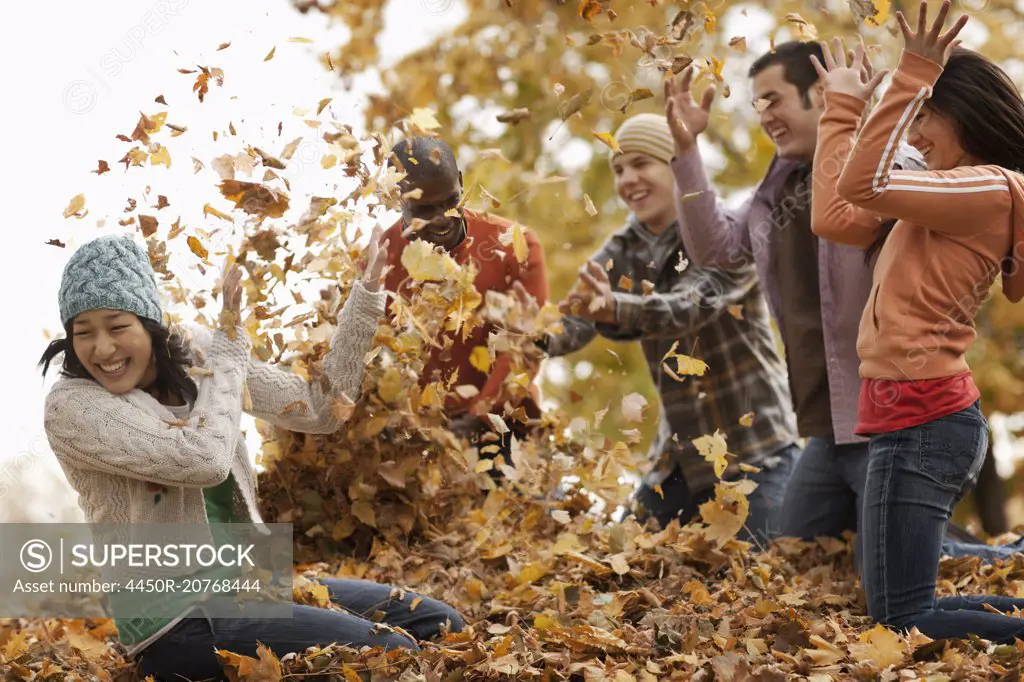 A group of men and women throwing fallen autumn leaves in the air