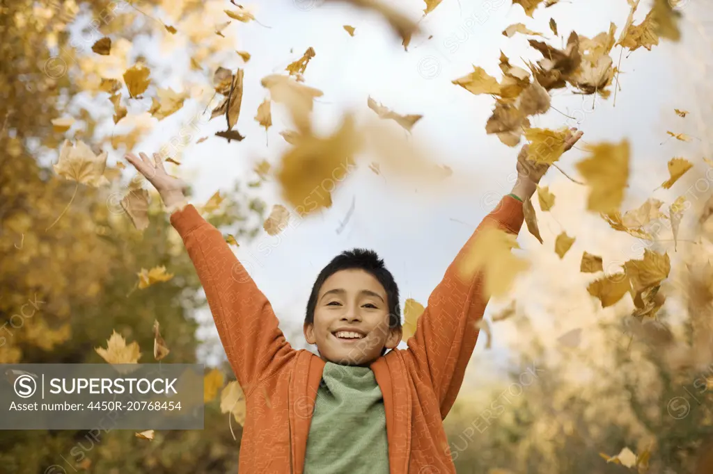 A boy throwing handfuls of fallen autumn leaves in the air