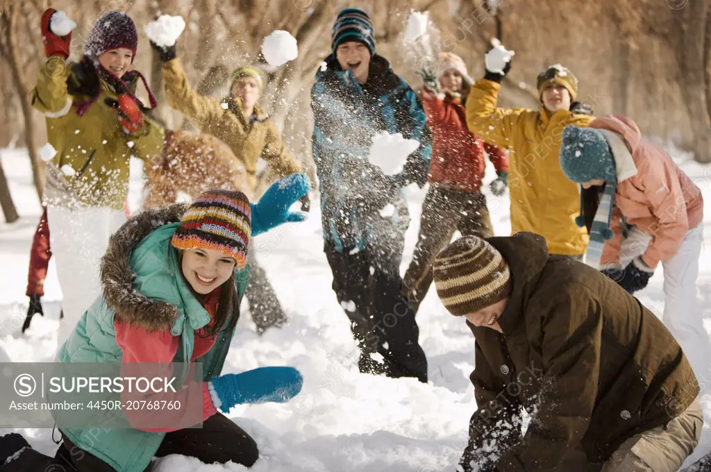 A group of young people, boys and girls having a snowball fight.