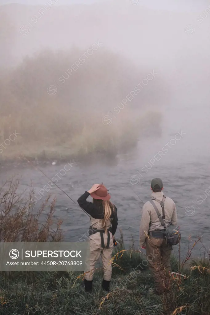 Two people, man and woman standing on the riverbank looking across the water.