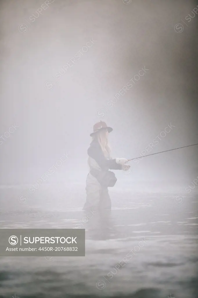 A woman fisherman flyfishing, standing in waders in thigh deep water.