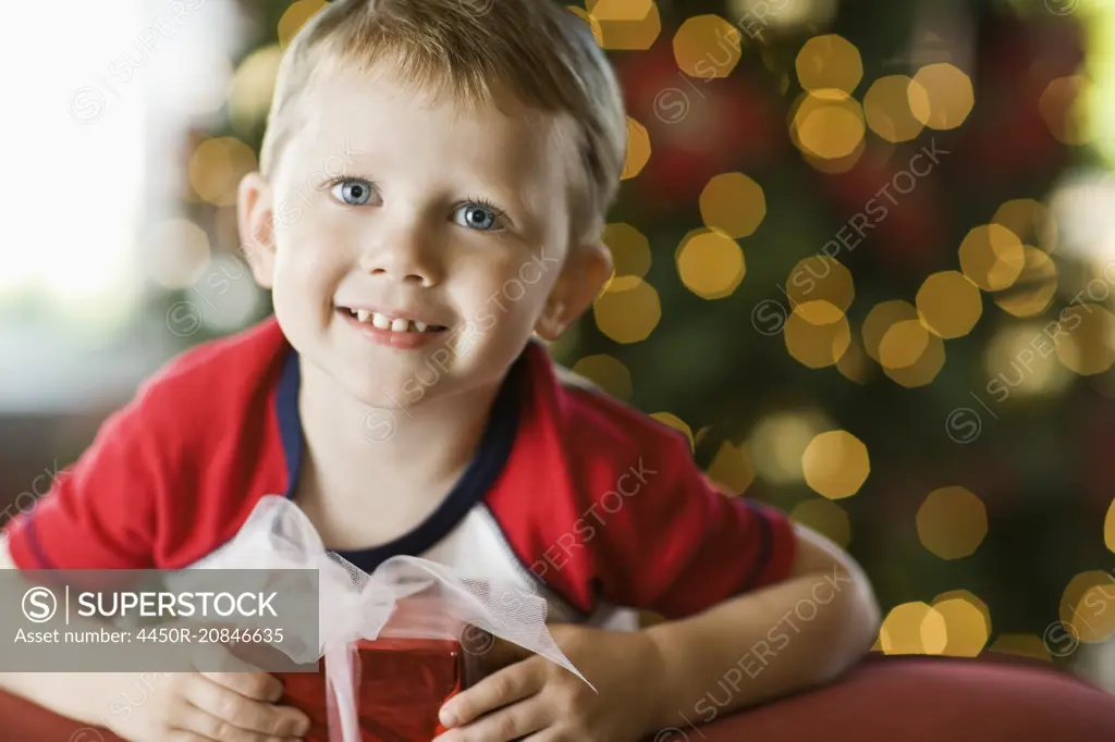 A small boy by a Christmas tree, holding a present.