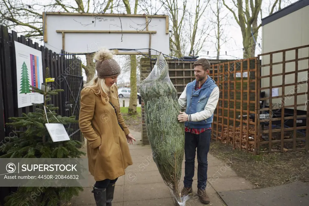 A member of staff carrying a traditional pine tree, Christmas tree talking to a woman client.