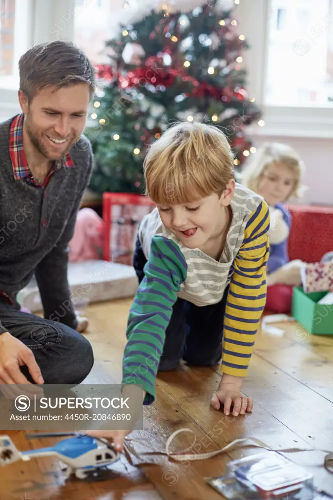 A man and two children finding and unwrapping presents on Christmas day.