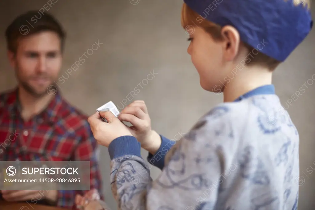 A man and a child seated at a kitchen table sharing a cracker joke.